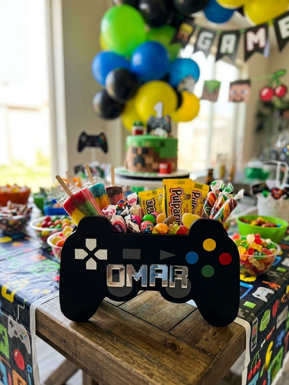 Ejemplo de prodcuto lleno de dulces en una mesa con fondo de fiesta cumpleañera. Cajas dulceras personalizadas con forma de control de videojuegos hechas en madera MDF calada a láser y pintadas a mano. Ideal para fiestas temáticas de gamers, centros de mesa y lapiceros de escritorio de niños.